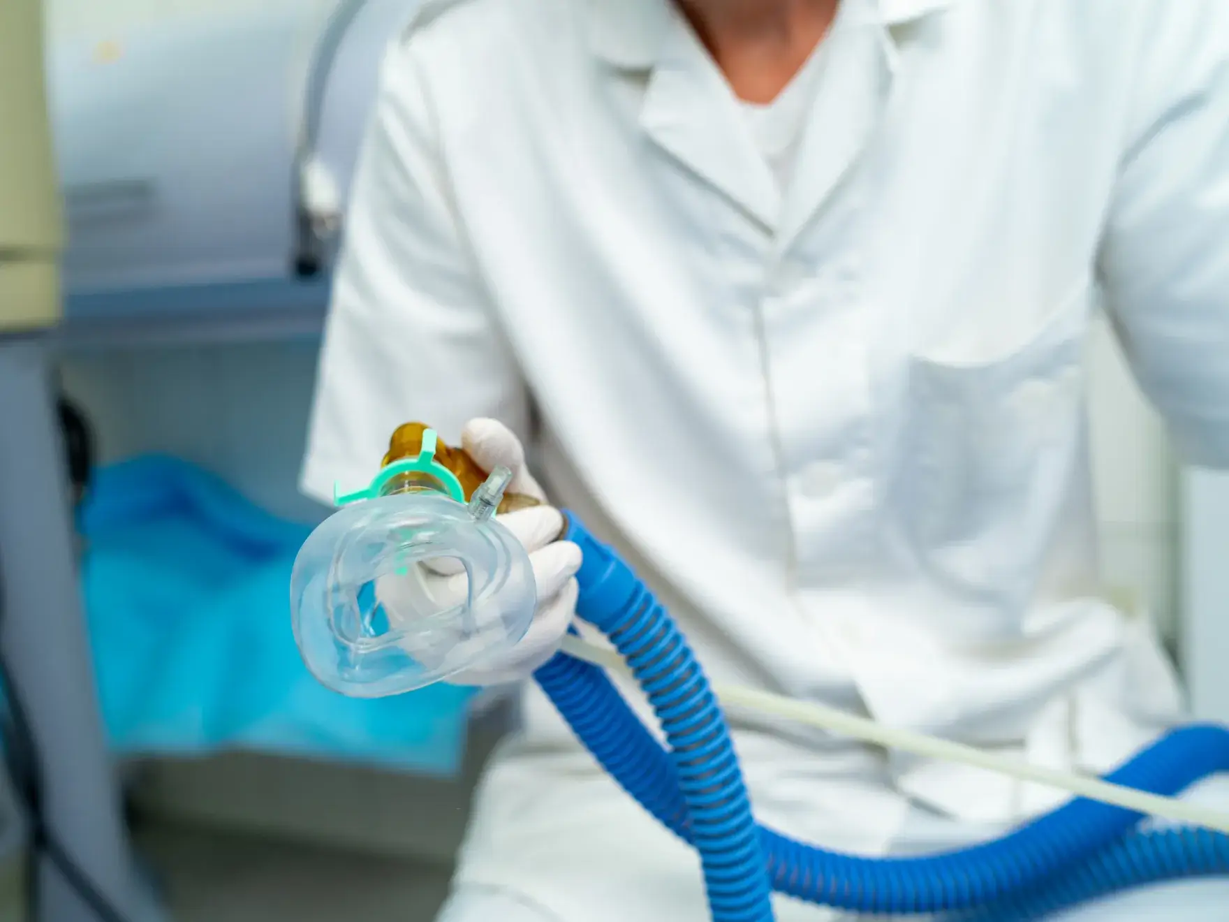 A person in medical attire holding a respiratory mask with a blue hose.